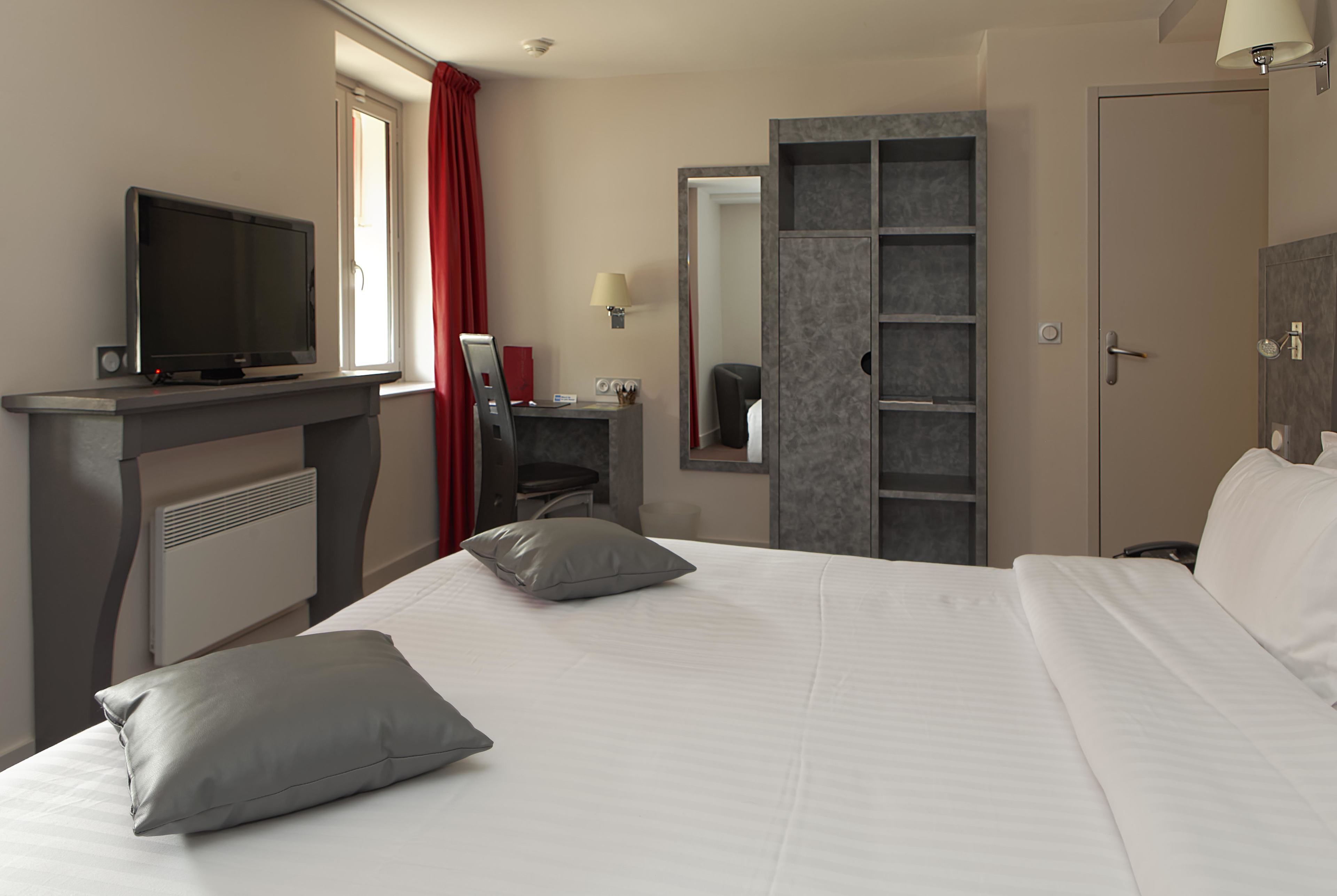 A hotel room with a bed, a desk with a television, a wardrobe, and a bathroom with a mirror.