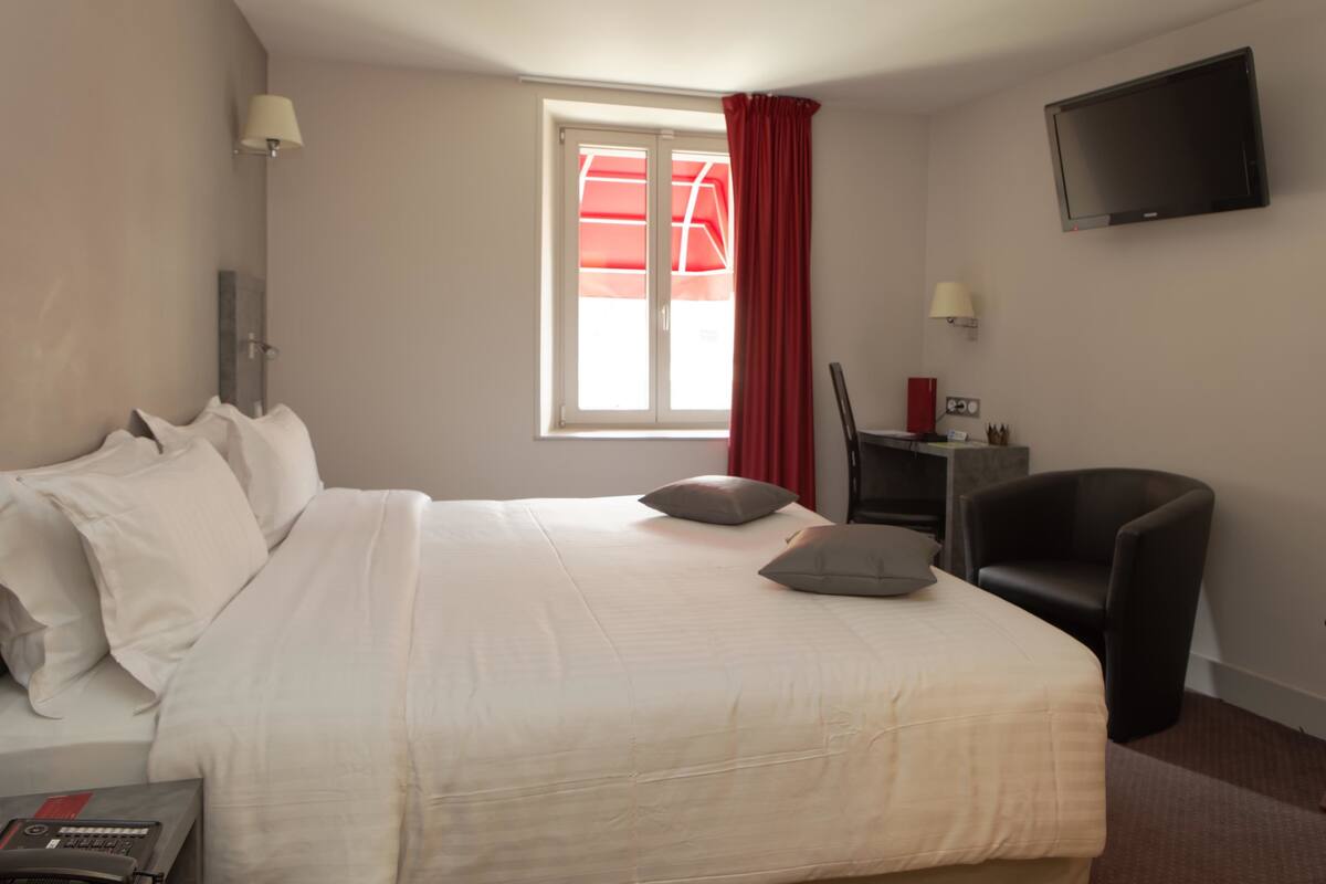 Una habitación de hotel con una cama, un escritorio con una silla, un televisor y una ventana con cortinas rojas.