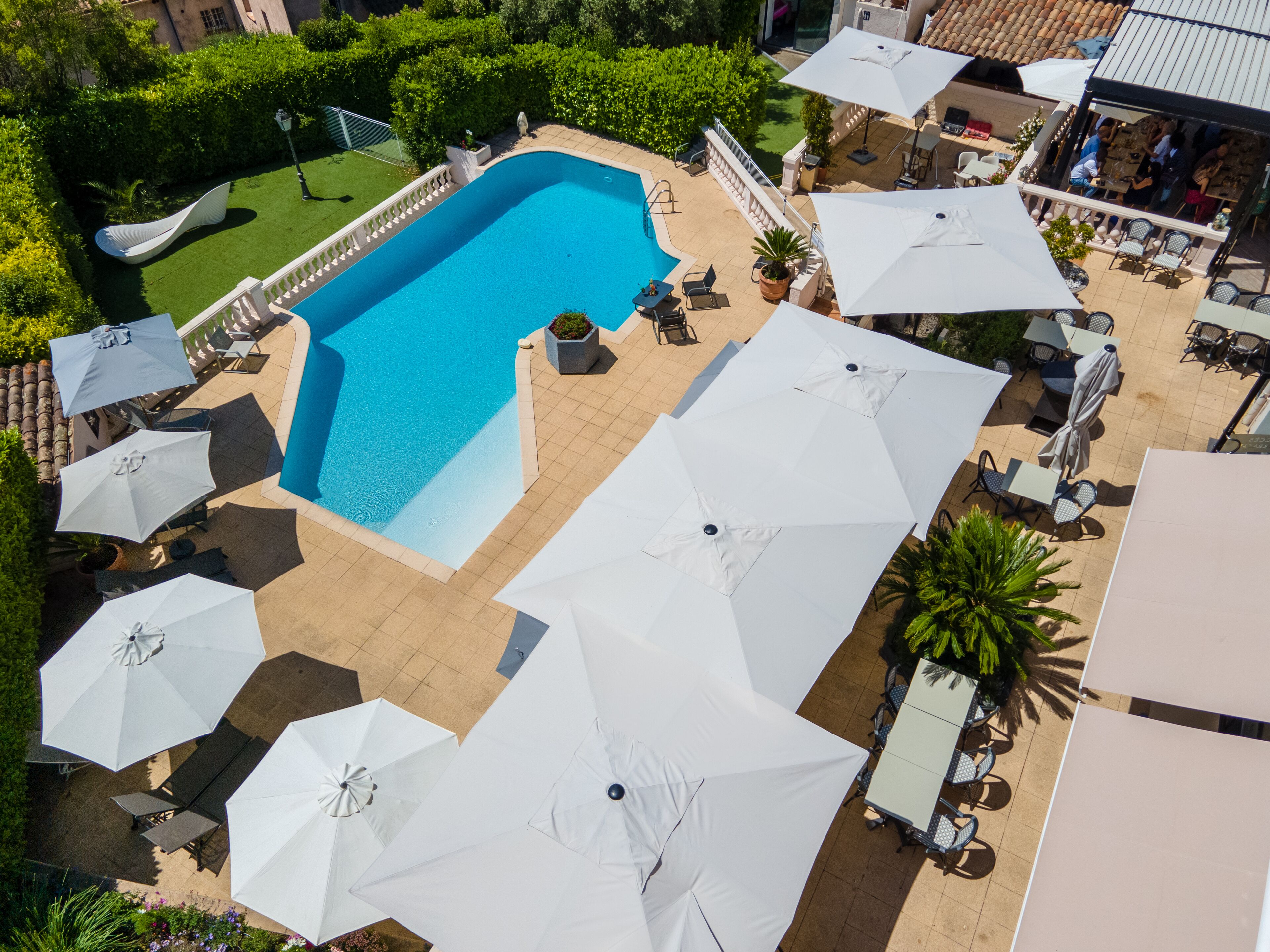 Una piscina rodeada de asientos al aire libre y sombrillas, con un patio y vistas de la vegetación circundante.