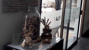 A reception area with a glass display case containing corks and decorative items, a wall-mounted corkboard, and a view of the outdoor area through large glass doors. - Hotel Perla Riviera (Cagnes-sur-Mer)