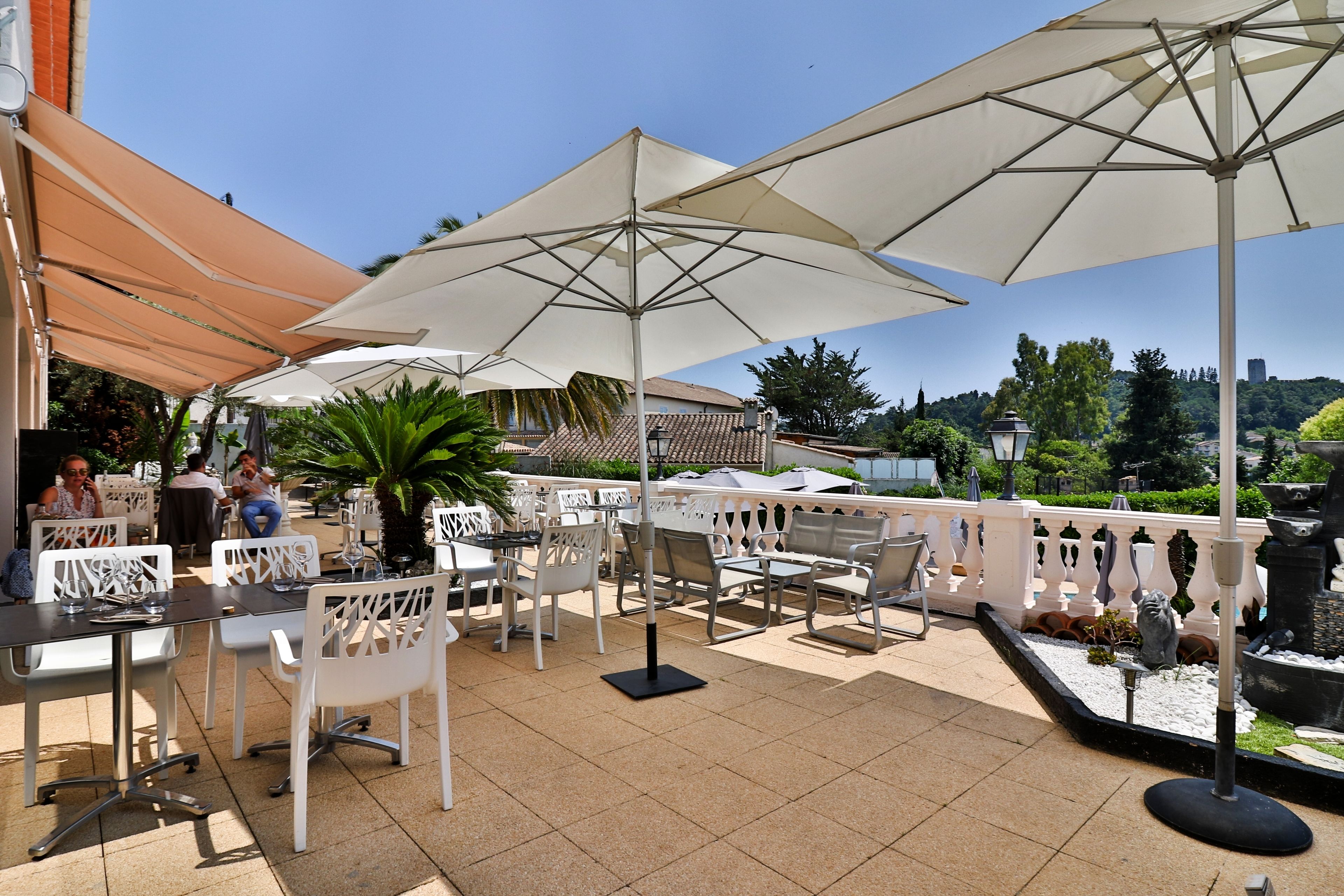 An outdoor patio with white chairs and tables, large umbrellas, and a view of a cityscape.