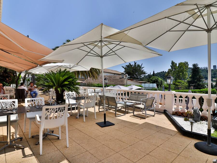 An outdoor patio with white chairs and tables, large umbrellas, and a view of a cityscape.