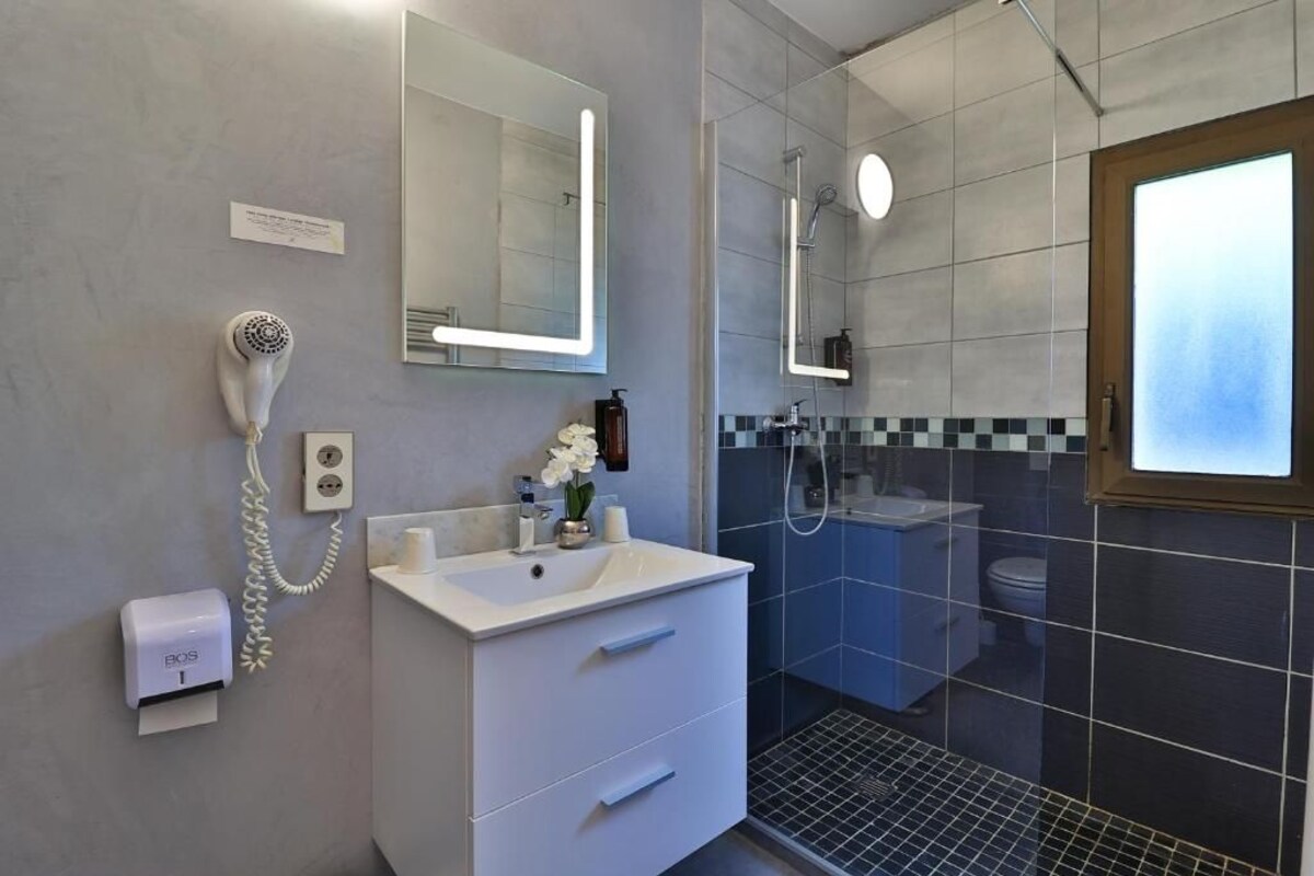 Un baño moderno con tocador blanco, secador de pelo, espejo y zona de ducha.