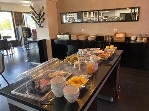 A buffet setup with various food items and beverages, a wine rack, and a counter with plates and utensils.