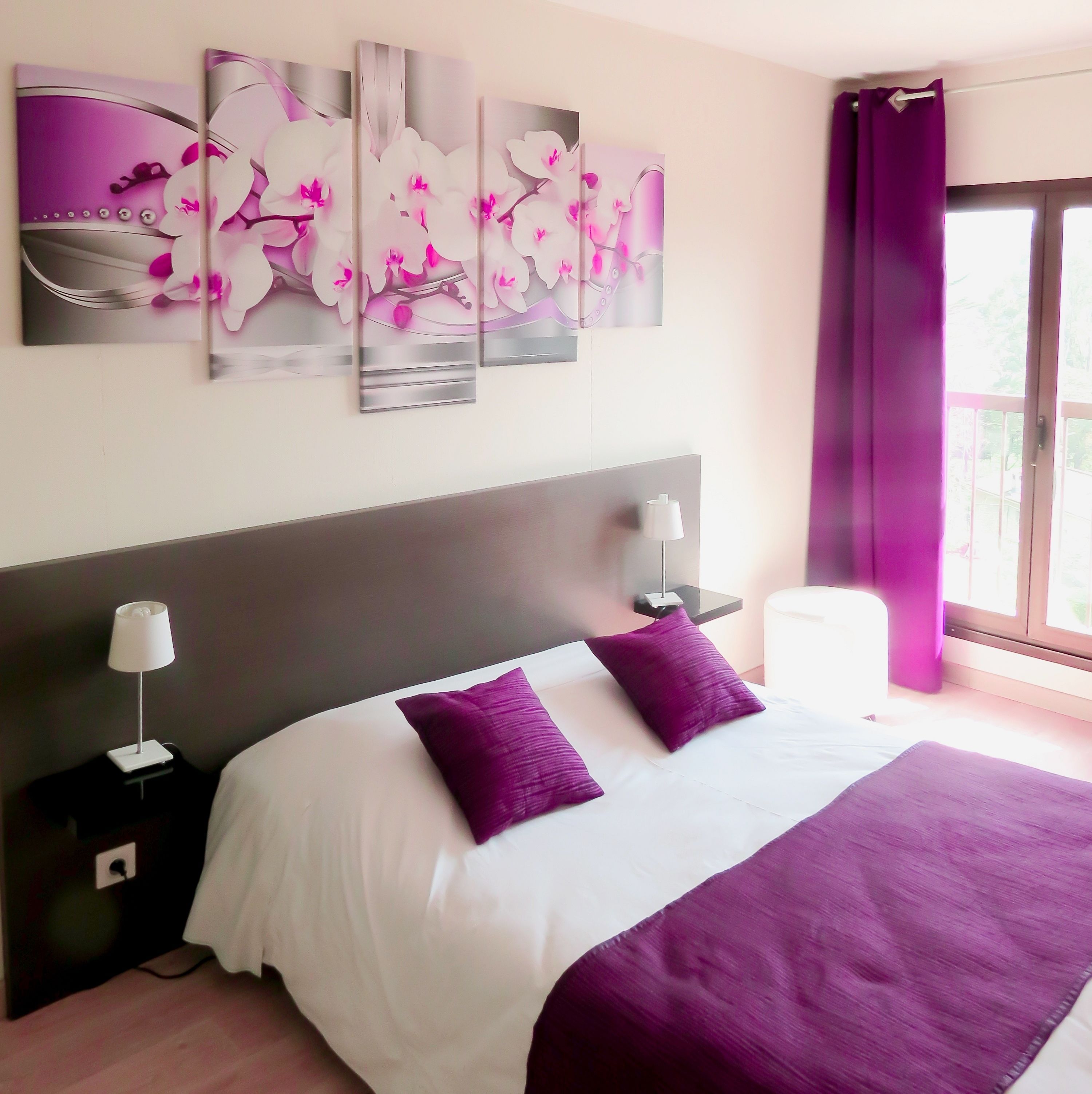 A bedroom with a large bed, two nightstands, a modern headboard, and a window with purple curtains.