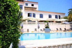 A swimming pool with lounge chairs and umbrellas, surrounded by a building with multiple windows and balconies.