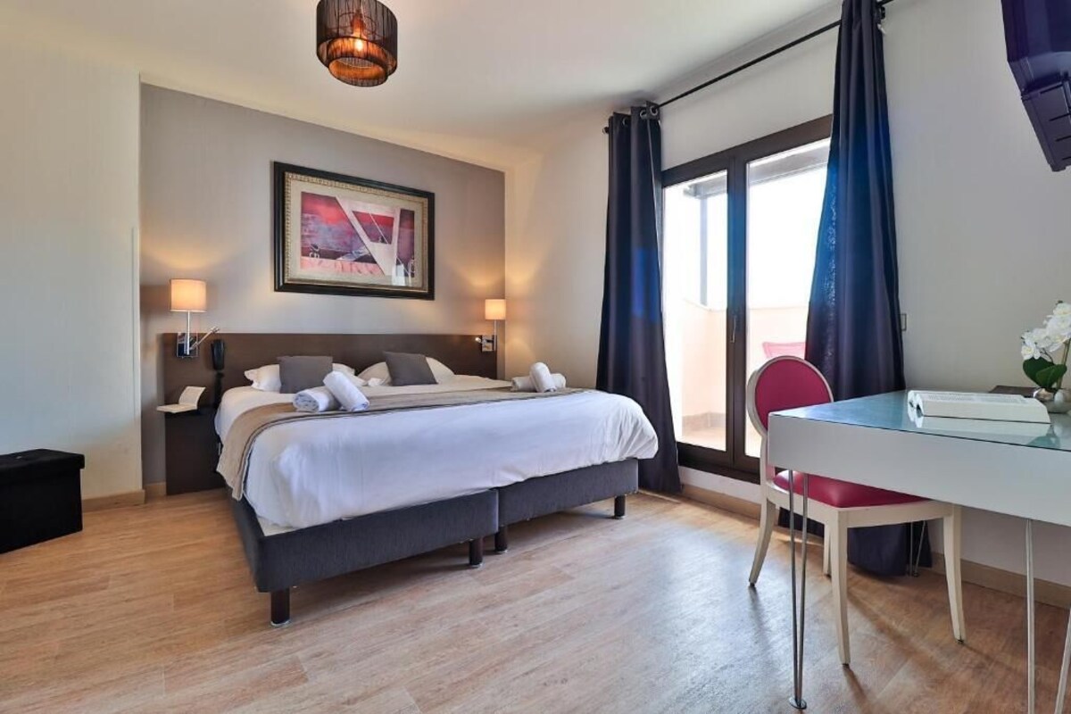 Una habitación de hotel moderna con una cama, lámparas de noche, un escritorio y un ventanal con cortinas.