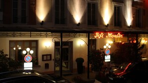 A hotel facade at night with illuminated signs, a no parking sign, and a car parked in front. - Hôtel Fifi Moulin (Serres)