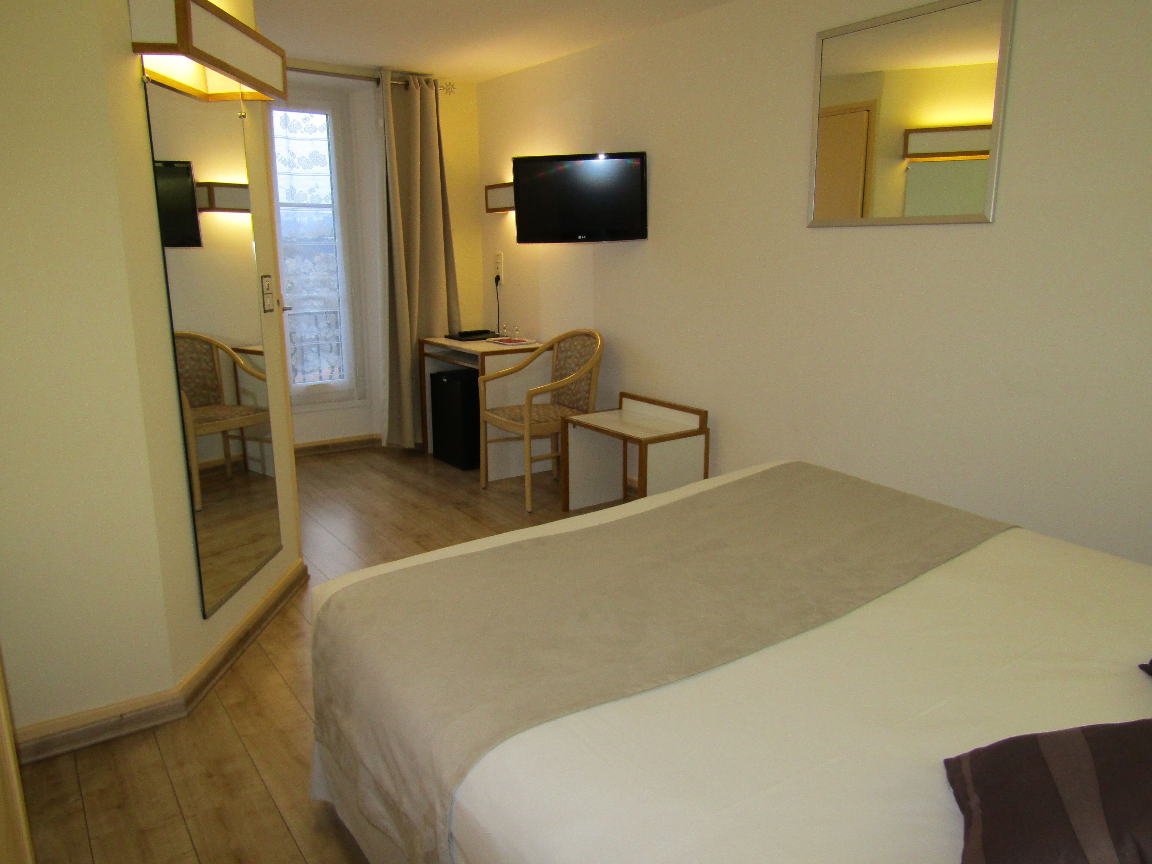 A hotel room with a bed, a desk, a chair, a TV, and a mirror.