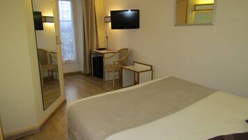 A hotel room with a bed, a desk, a chair, a TV, and a mirror.