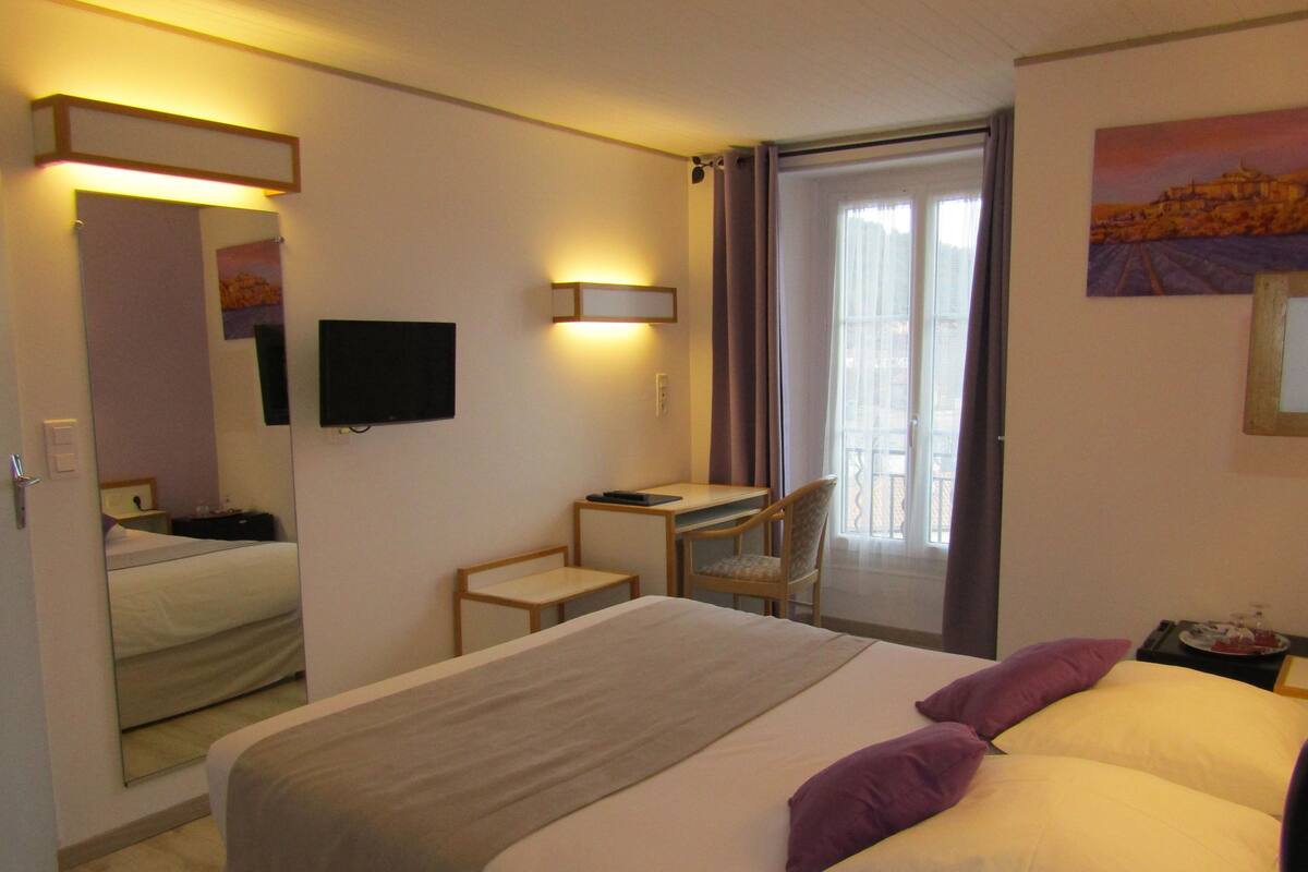 A hotel room with a bed, a desk, a chair, a television, and a window with curtains.
