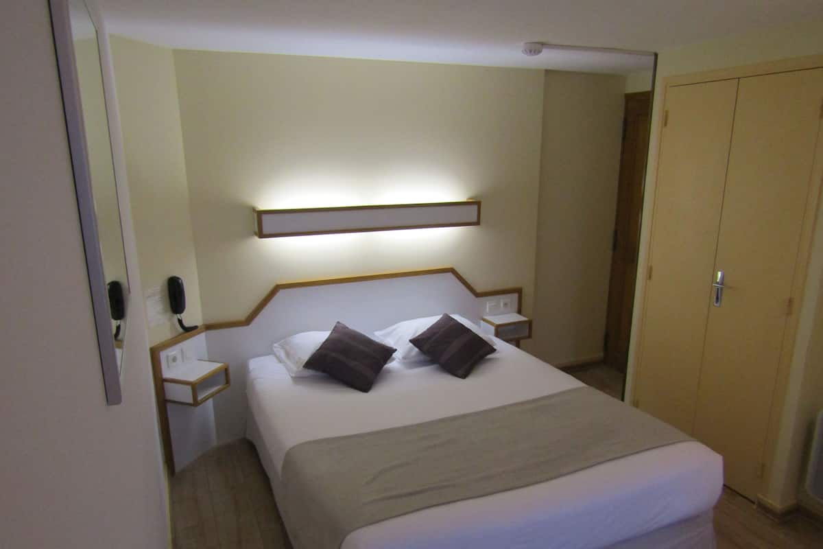 A hotel room with a bed, bedside tables, a nightstand, a mirror, and a wardrobe.