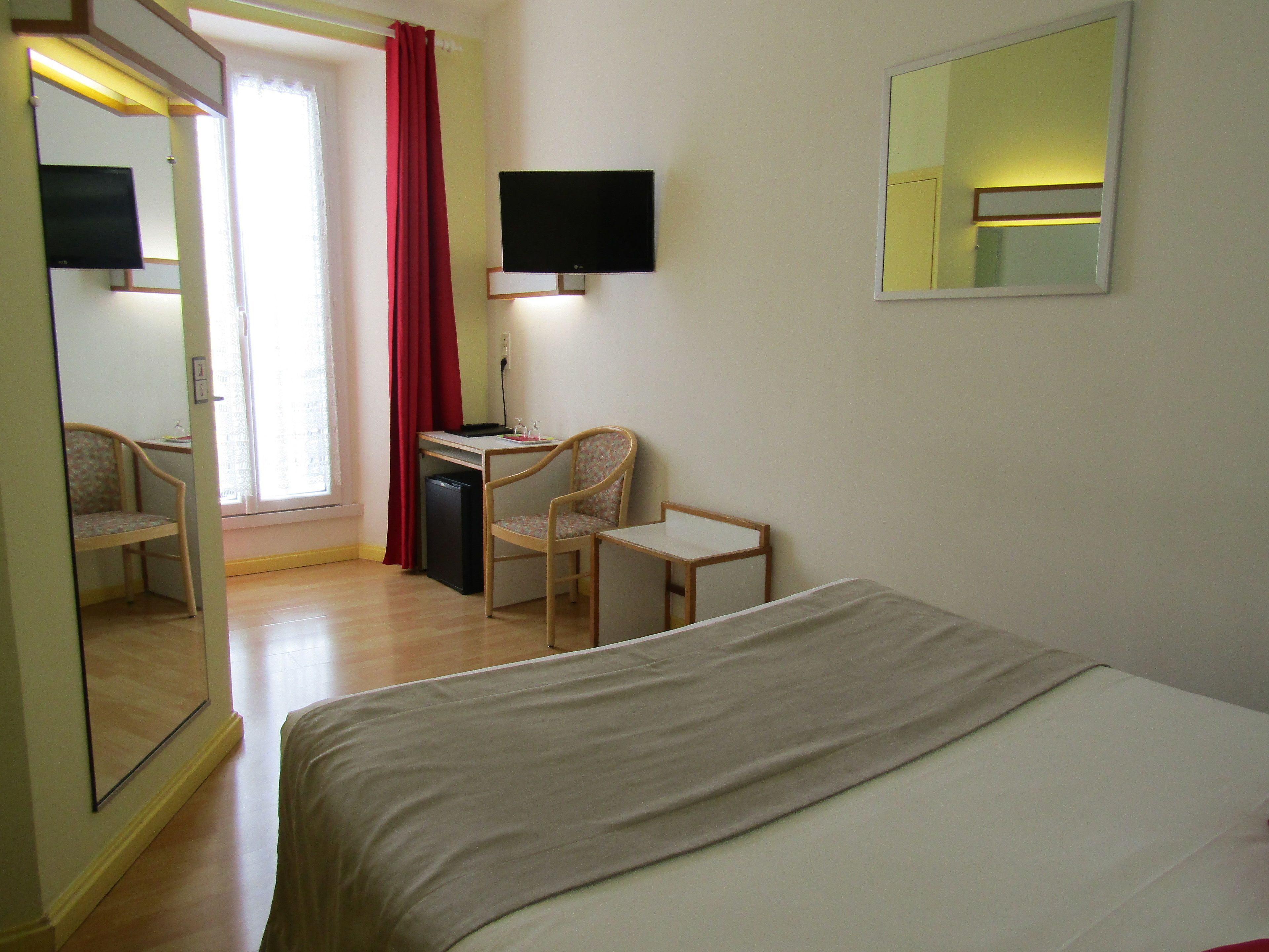 A hotel room with a bed, a desk with a chair, a television, and a mirror.