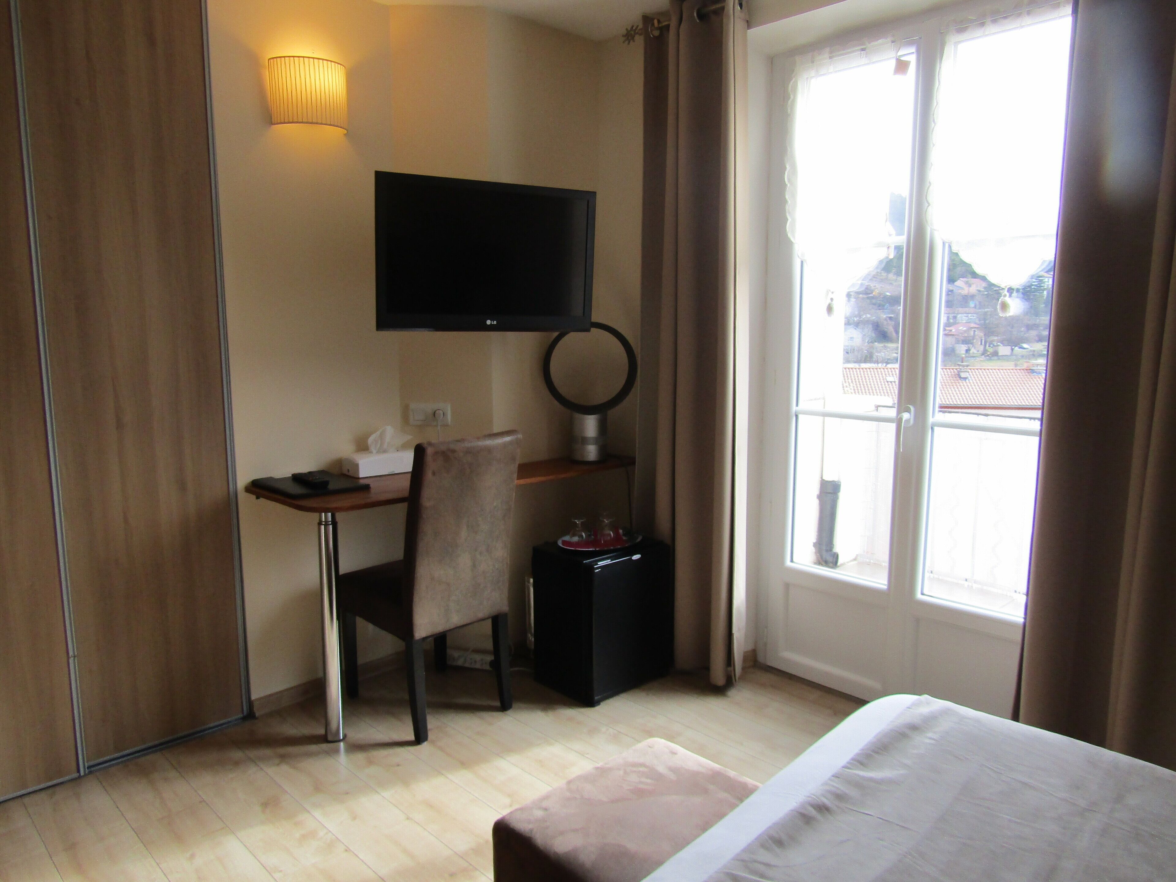 Ein Hotelzimmer mit Bett, Schreibtisch mit Stuhl, Wandfernseher, kleinem Tisch mit Taschentuchbox und einem Vorhangfenster.