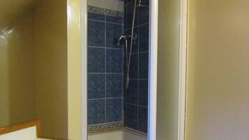 A small, enclosed shower area with a tiled floor and walls, a wooden bench, and a white sink.