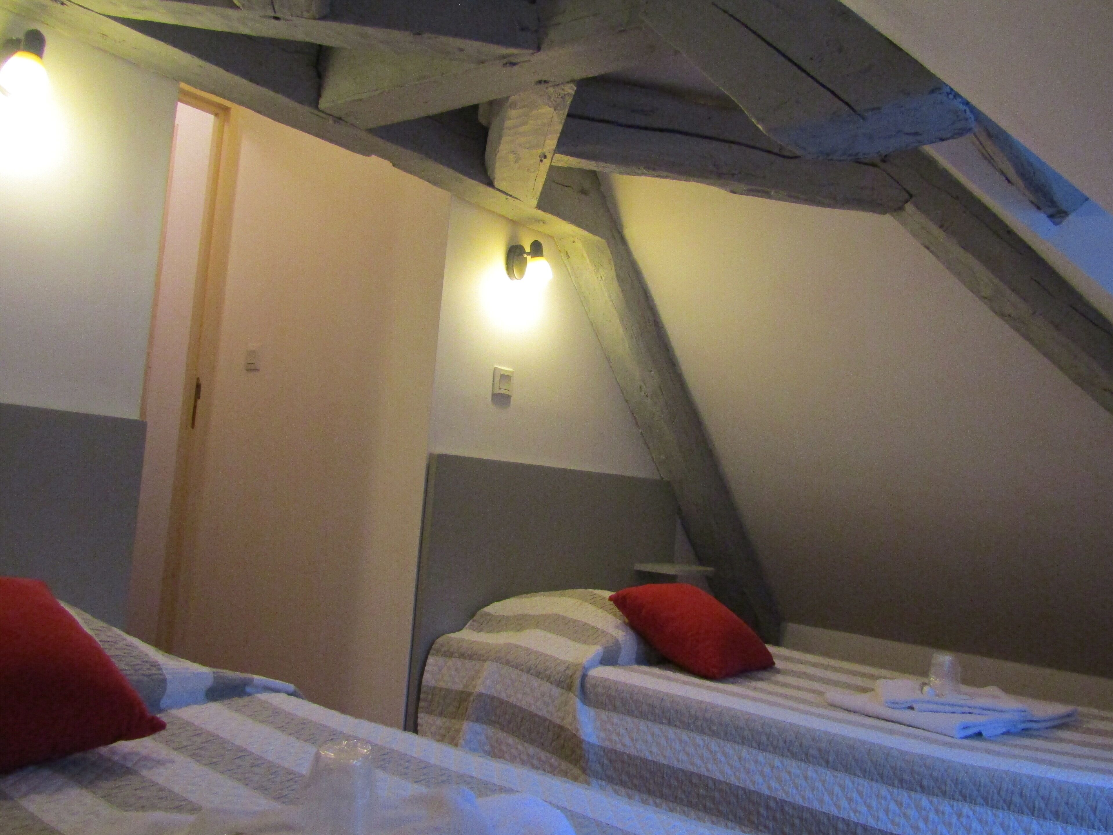 A room with two beds, each with a red pillow, a wooden ceiling, and a light fixture on the wall.
