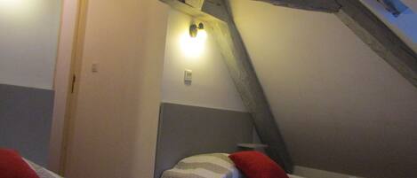 A room with two beds, each with a red pillow, a wooden ceiling, and a light fixture on the wall.