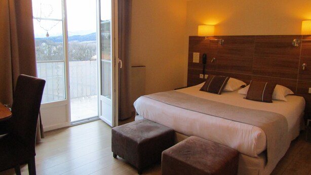 A hotel room with a large bed, two bedside tables, a chair, and a view through a sliding glass door. - Hôtel Fifi Moulin (Serres)