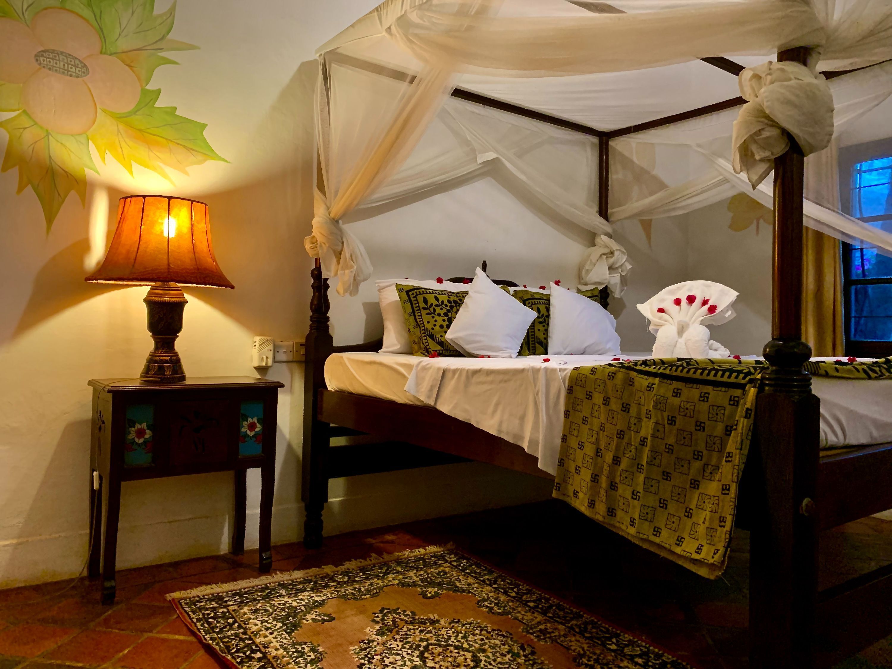 A four-poster bed with a canopy, a bedside table with a lamp, and a patterned rug.