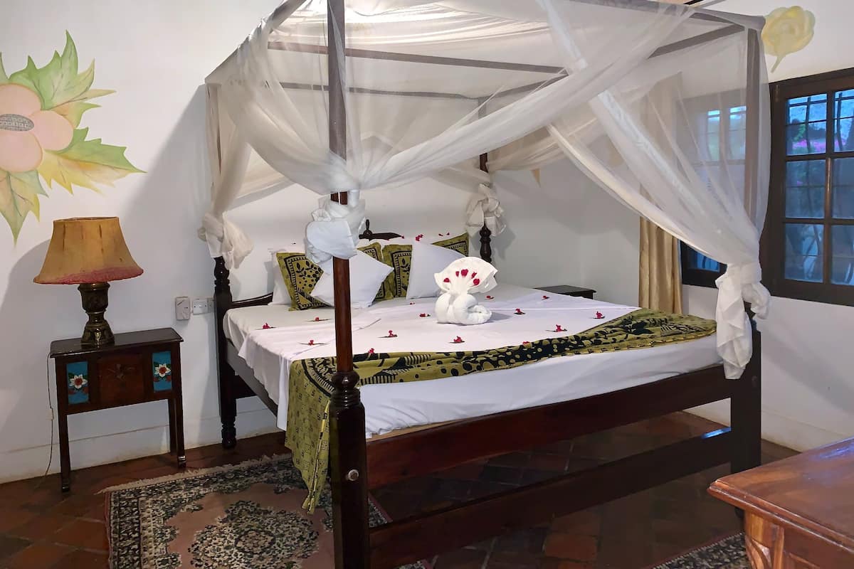 Una cama con dosel, una mesita de noche con lámpara, almohadas estampadas y una toalla decorativa.