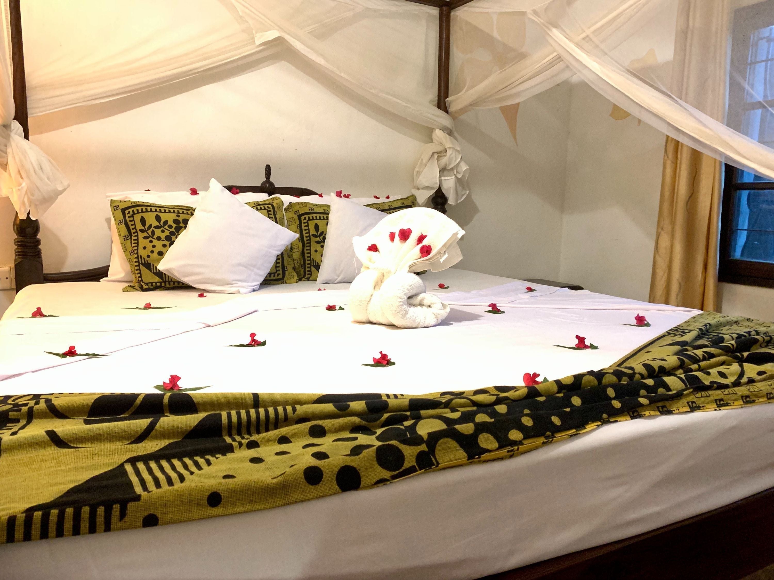 A bed with a white sheet, a yellow and black patterned blanket, and a white pillow with a red flower.