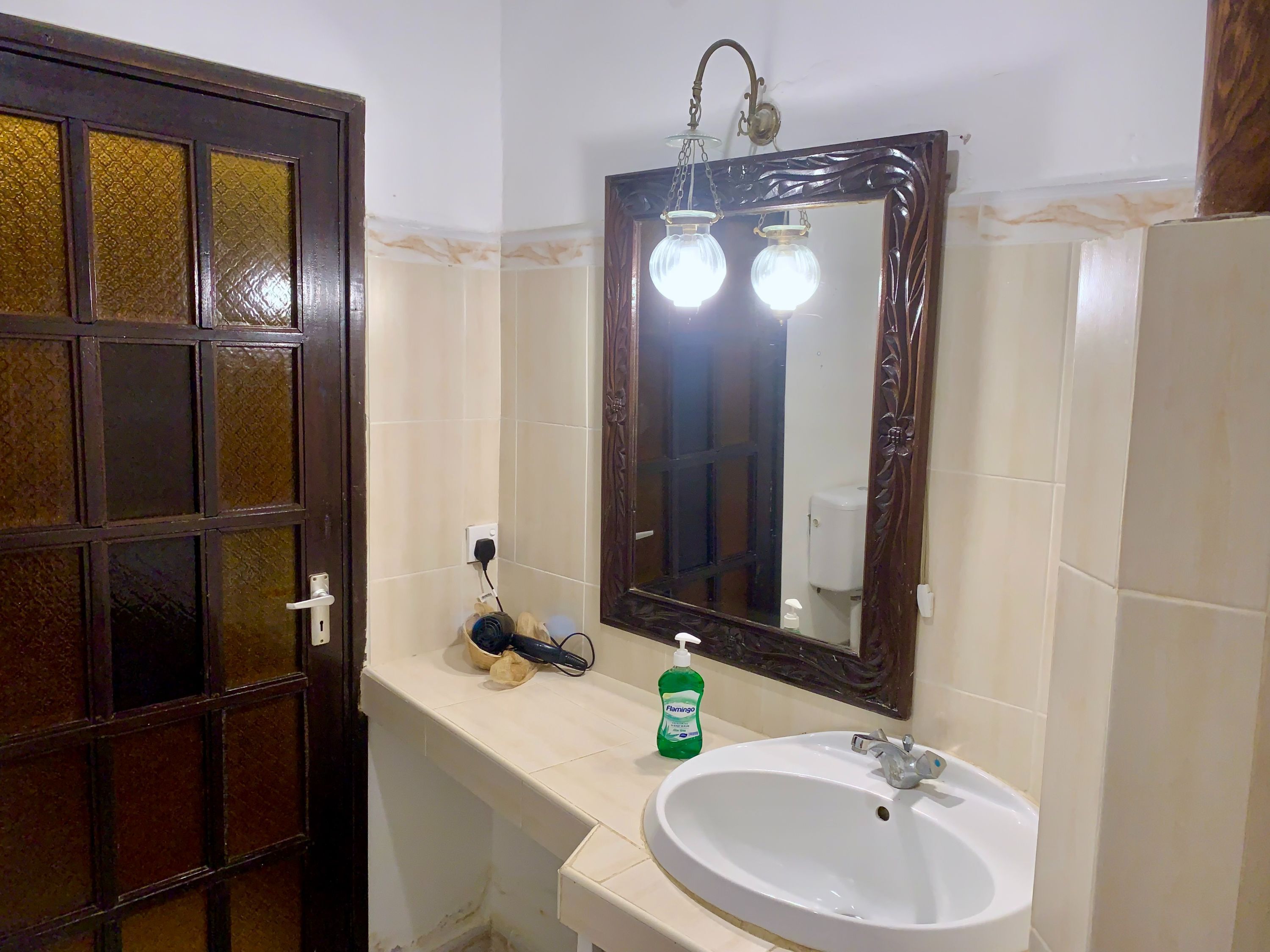 Une salle de bain avec un lavabo blanc, un miroir avec éclairage intégré, une porte avec un panneau de verre et des toilettes.