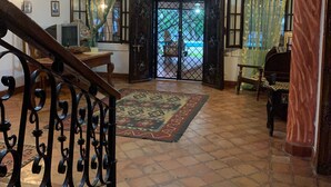 A spacious living area with a tiled floor, a staircase with ornate railings, a ceiling fan, and a view through a glass door to an outdoor area. - Kenyan House Malindi (Malindi)