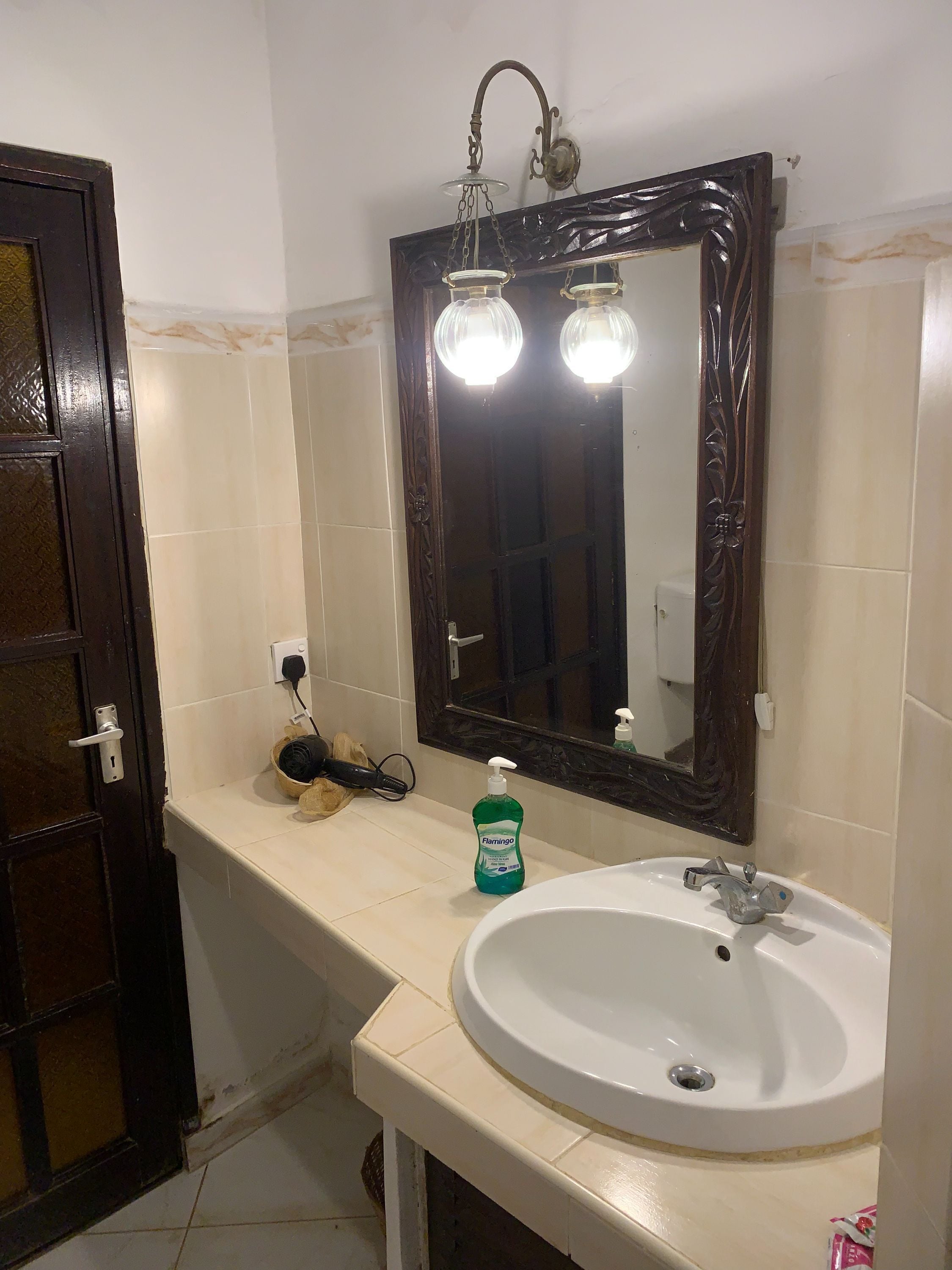 Un baño con un lavamanos blanco, un espejo con dos luces y una puerta de madera oscura.