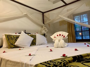 Un lit avec des oreillers blancs et à motifs, un objet décoratif blanc qui ressemble à un cygne, et des pétales de roses rouges éparpillés.