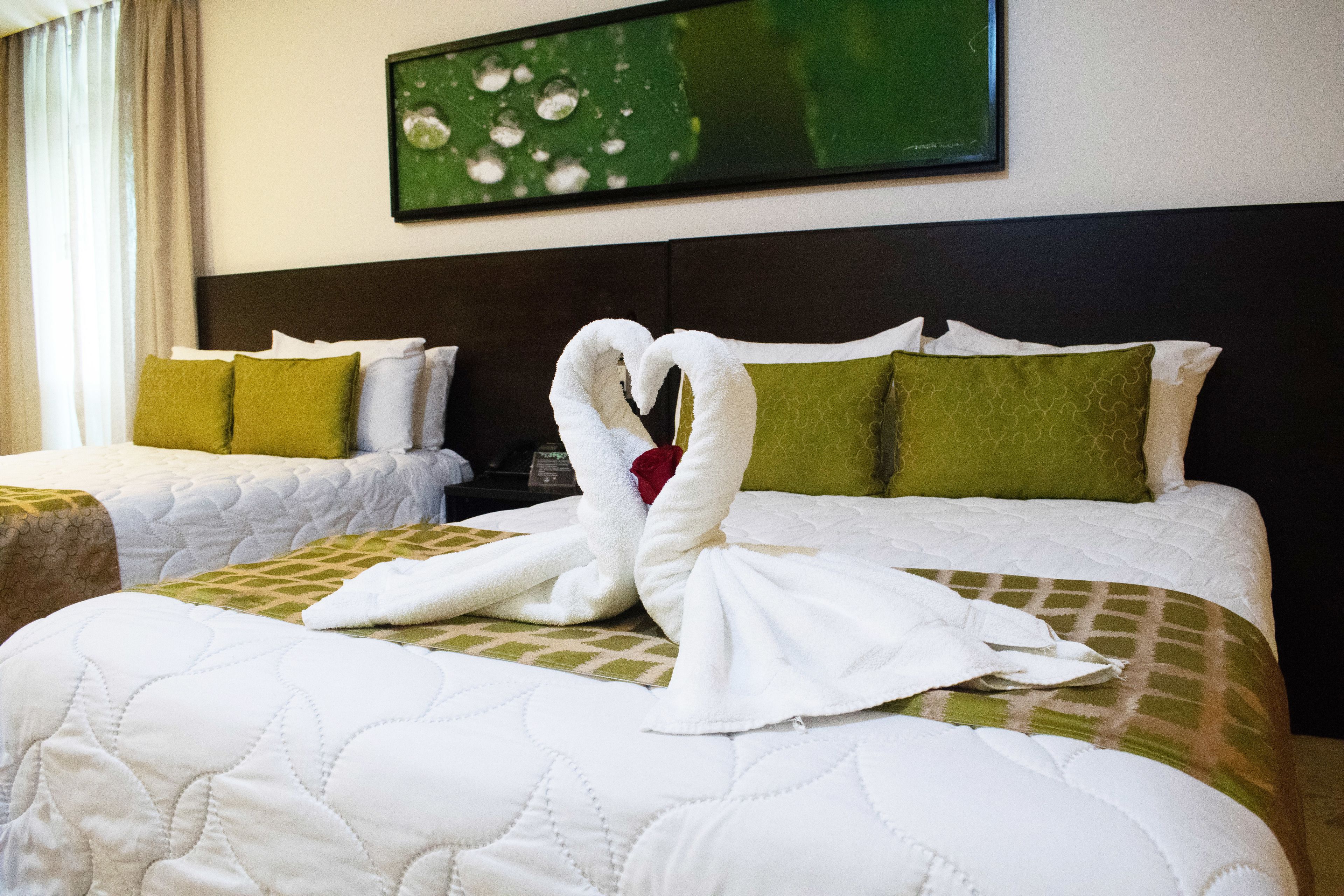 Ein Hotelzimmer mit zwei Betten, eines mit einer grün-weißen Bettdecke und das andere mit einer schlichten weißen Bettdecke. Darüber an der Wand hängt ein Bild.