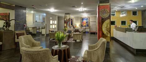 A hotel lobby with seating areas, a reception desk, and artwork on the walls.