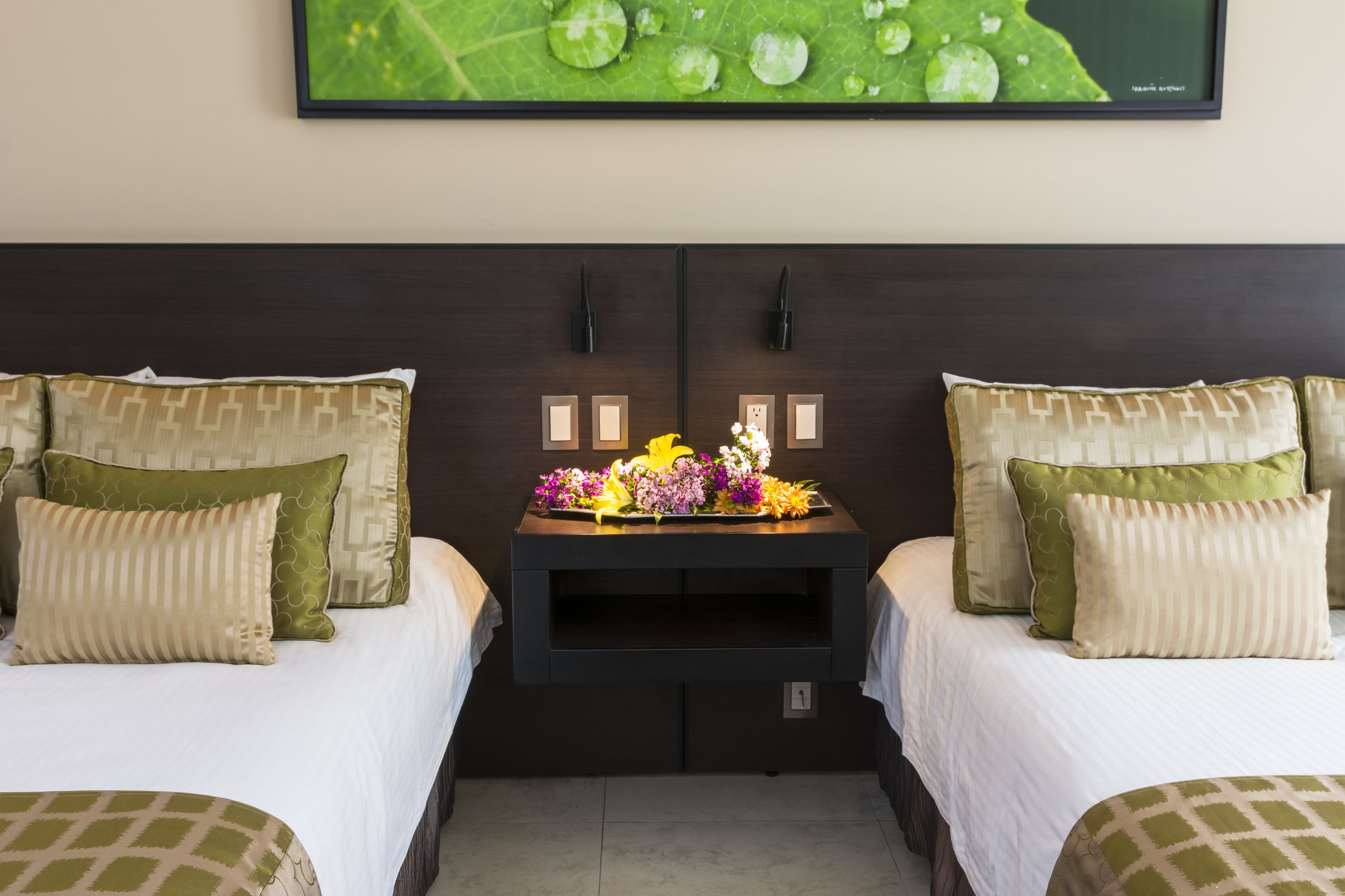 A hotel room with two beds, a nightstand with a floral arrangement, and a framed picture on the wall.