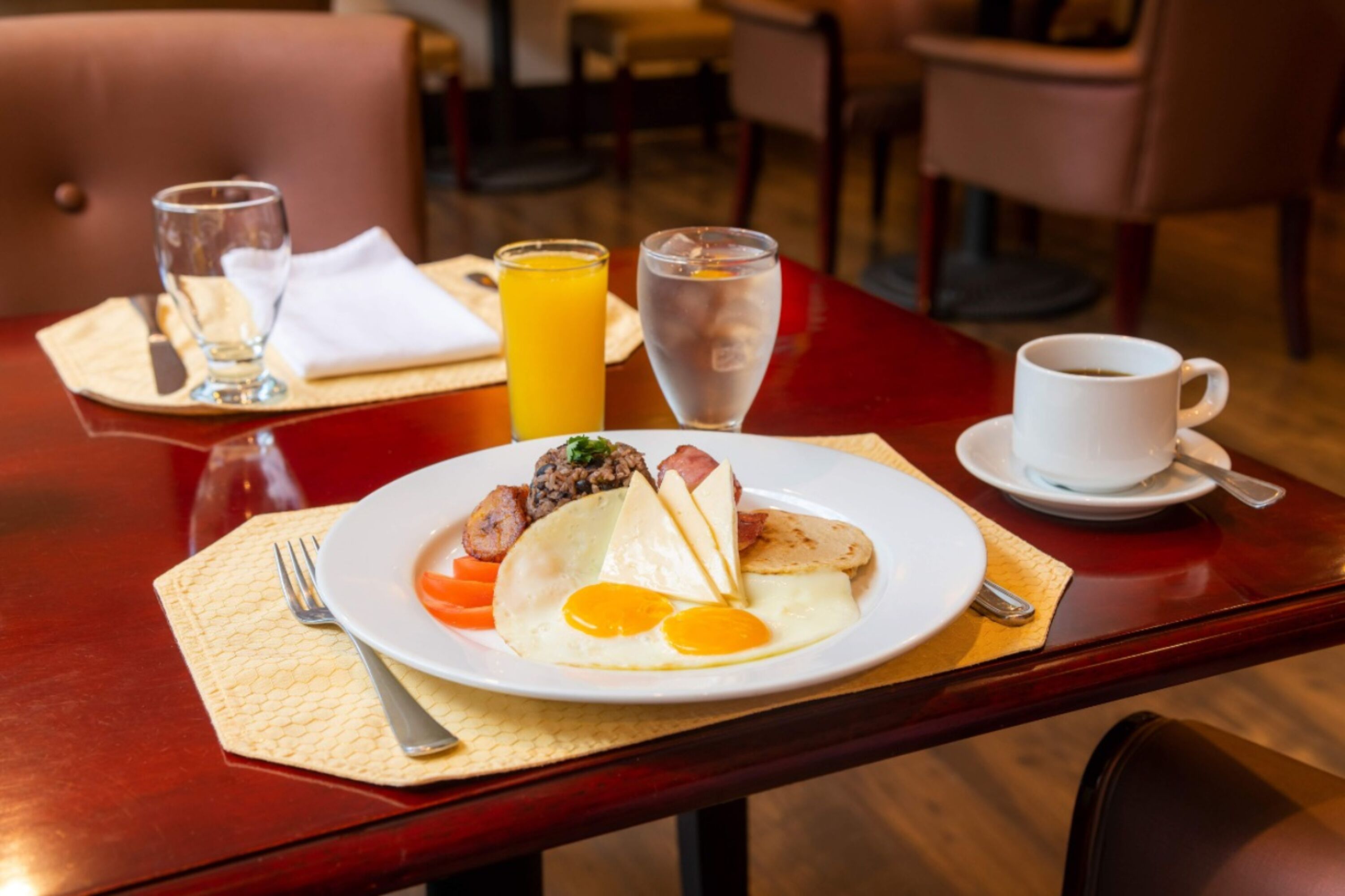 Ein Frühstückstisch mit Essen, Orangensaft, Wasser und einer Tasse Kaffee.