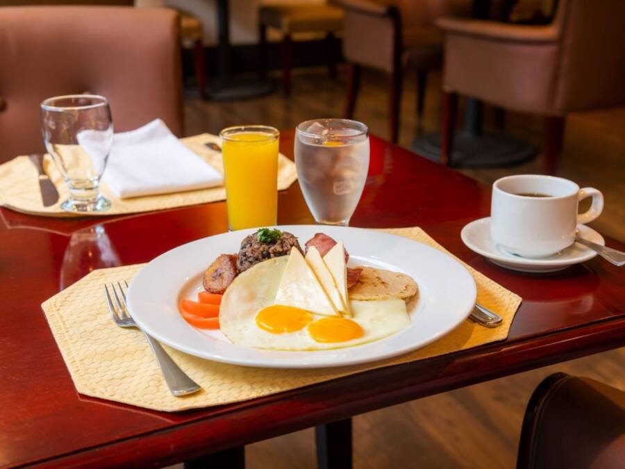 A breakfast setting with a plate of food, a glass of orange juice, a glass of water, and a cup of coffee on a wooden table.