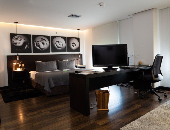 A modern bedroom with a bed, bedside tables, a desk, a chair, a television, and artwork on the wall. - Studio Hotel Boutique (Santa Ana)