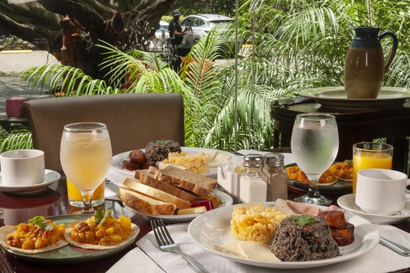 A breakfast setting with various dishes, including toast, scrambled eggs, and rice, on a table with a view of a lush garden.