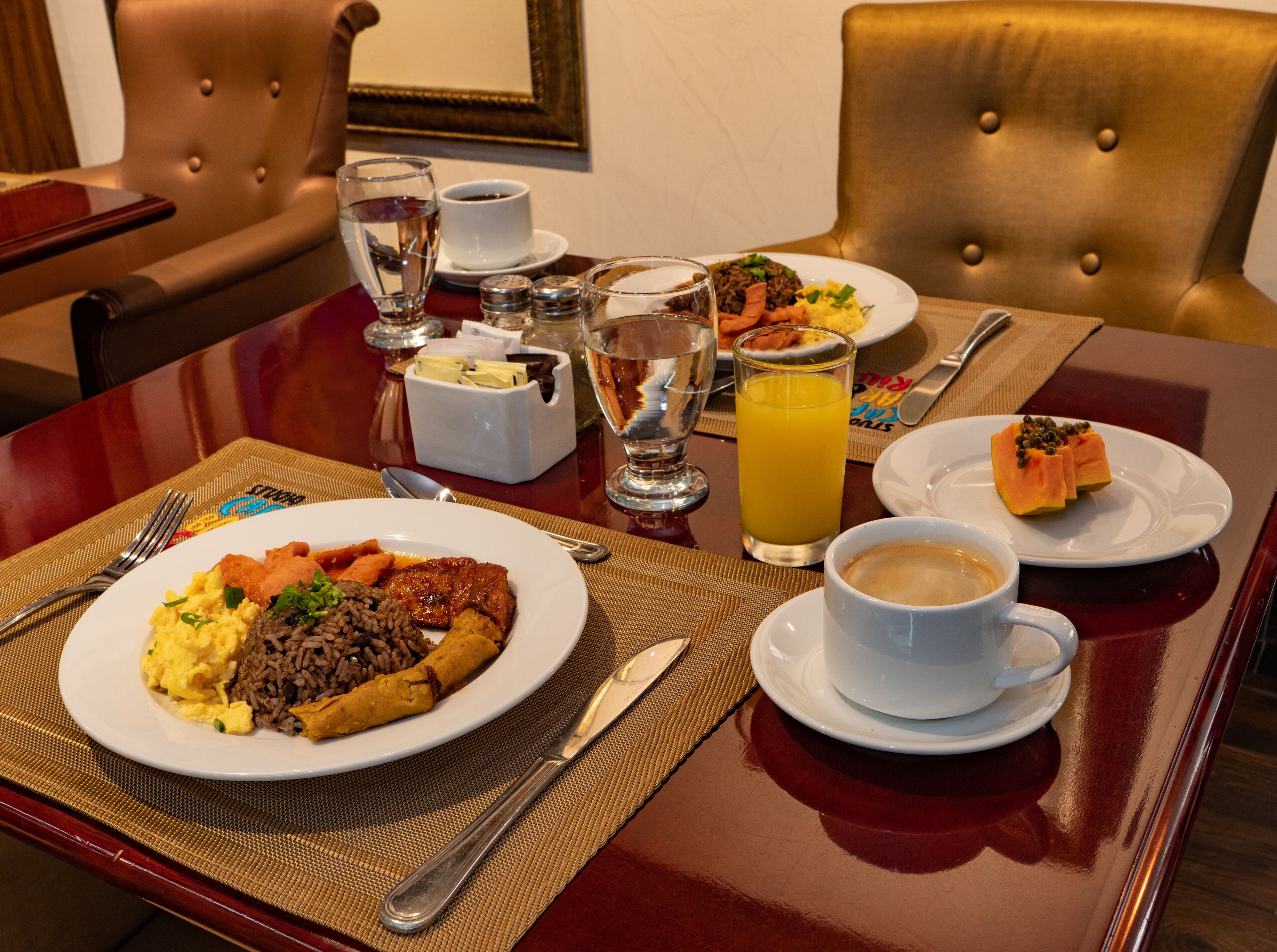 A dining table with a variety of dishes, including a plate of scrambled eggs, rice, and meat, a glass of orange juice, and a cup of coffee.