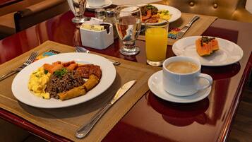A dining table with a variety of dishes, including a plate of scrambled eggs, rice, and meat, a glass of orange juice, and a cup of coffee.