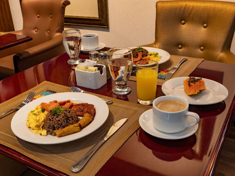 A dining table with a variety of dishes, including a plate of scrambled eggs, rice, and meat, a glass of orange juice, and a cup of coffee.