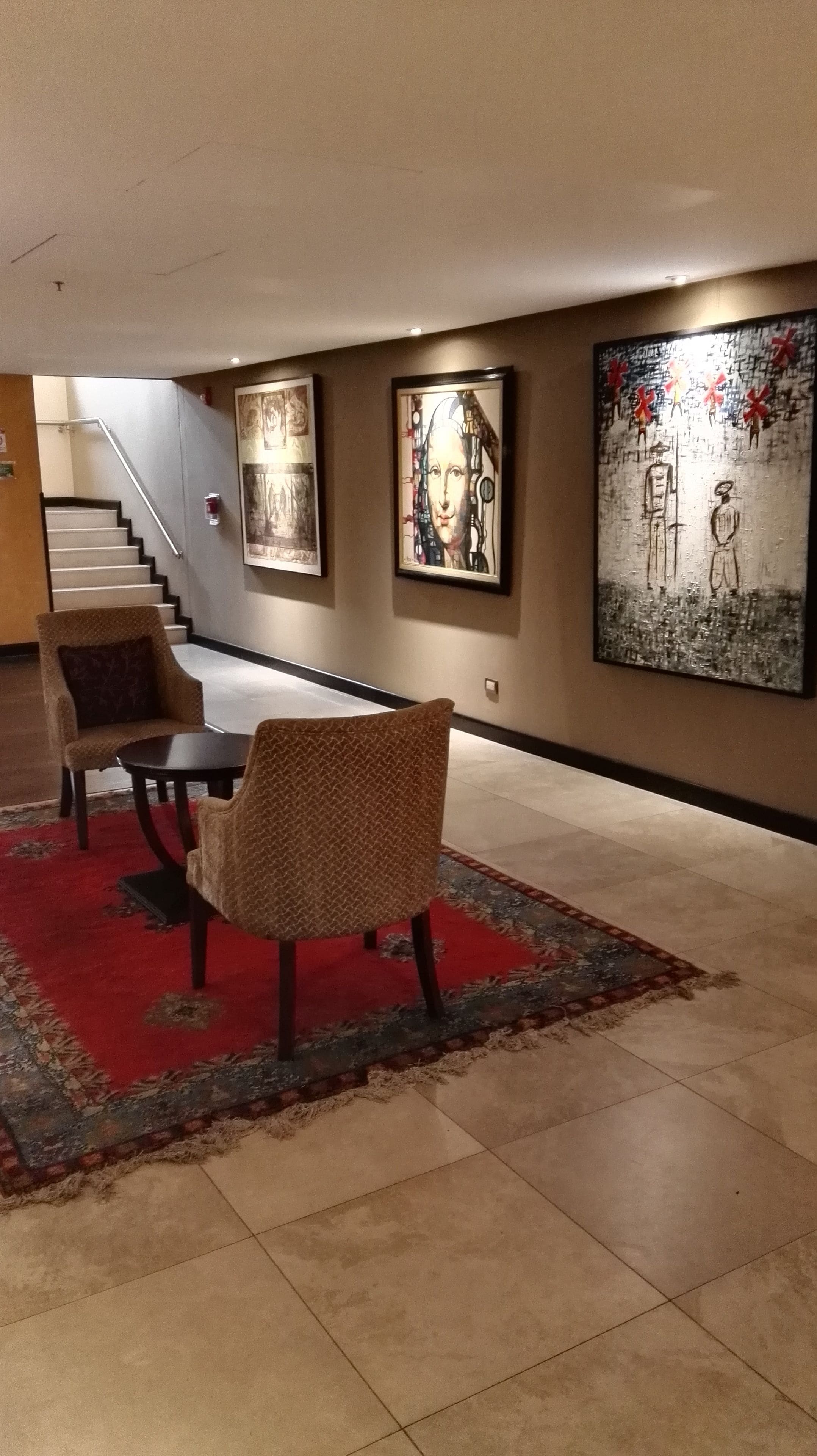 A dining area with a table and chairs, a staircase, and three framed artworks on the wall.