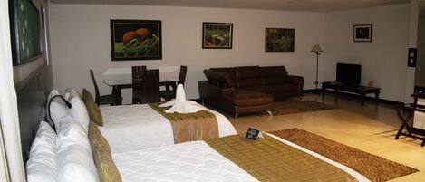 Una habitación de hotel con una cama grande, un sofá marrón, un escritorio con lámpara y cuadros en la pared.