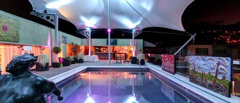A swimming pool with a covered area, tables, chairs, and artwork.