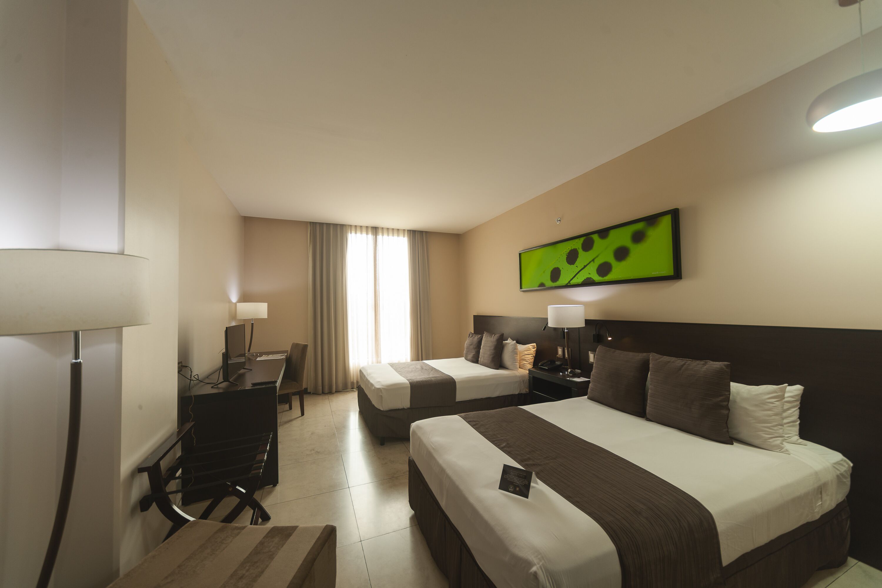 A hotel room with two beds, a desk, a chair, and a desk lamp.