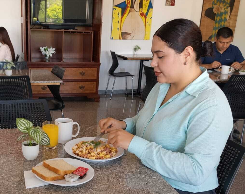 A person dining at a table with a meal, a coffee cup, and a plant.