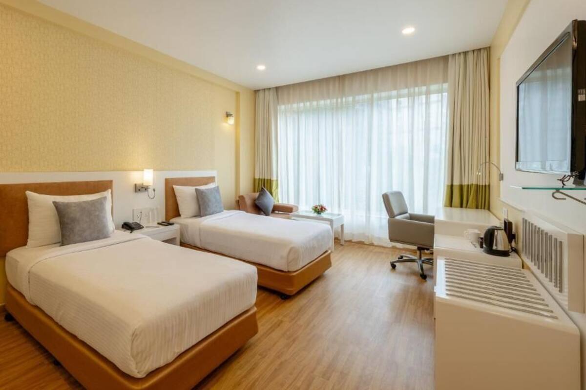 Habitación de hotel con dos camas, un escritorio, una silla, un televisor y una ventana con cortinas.
