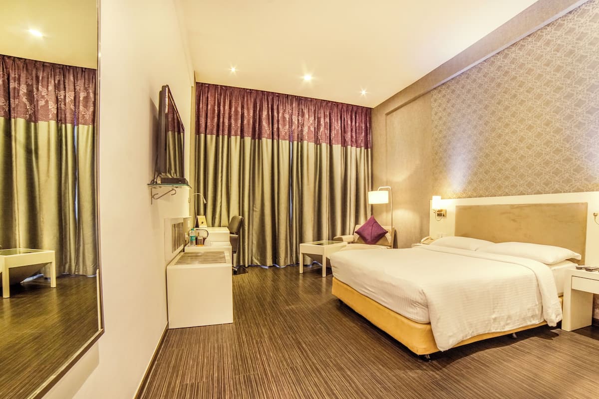 Una habitación de hotel con cama, mesitas de noche, espejo, cortinas y un papel tapiz estampado.