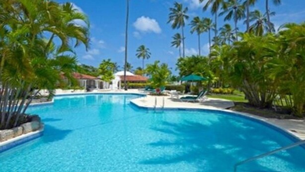 A clear blue swimming pool surrounded by palm trees and a white building with a red roof. - Glitter Bay (Holetown)