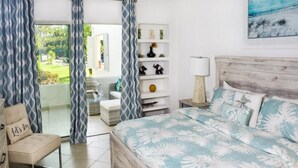A bedroom with a bed, a chair, a shelf with decorative items, and a view of the outdoors. - Glitter Bay (Holetown)