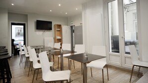 A modern dining area with white chairs and tables, a flat-screen TV, and large windows. - Enjoy Hostel (Paris)