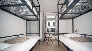 A dormitory room with bunk beds, a foldable chair, and a small table. - Enjoy Hostel (Paris)